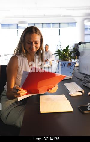 Smiling businesswoman reviewing documents at desk with laptop and charts Stock Photo