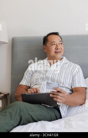 Relaxing at home, senior man using tablet and holding credit card, smiling Stock Photo