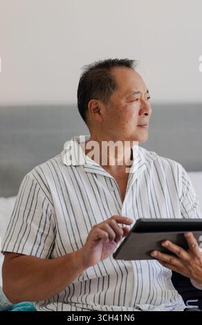 Senior man using tablet at home, looking thoughtfully out window Stock Photo
