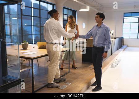 Business professionals shaking hands in modern office, collaborating on project Stock Photo