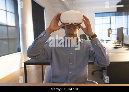 Businessman using VR headset at office desk, exploring virtual reality technology Stock Photo