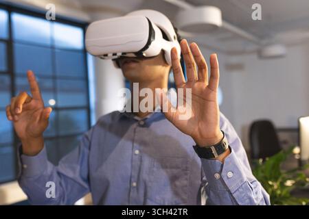 Businessman using VR headset in modern office, interacting with virtual environment Stock Photo