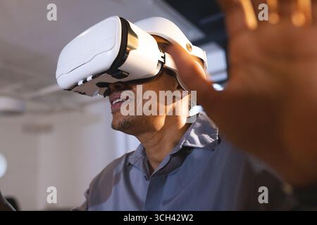 Using VR headset, African American man exploring virtual reality in office setting Stock Photo