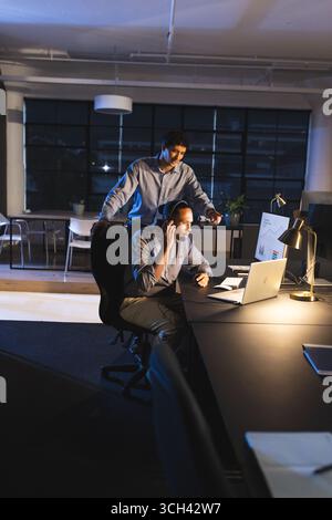 Businessmen working late in office, discussing project on laptop with focus Stock Photo
