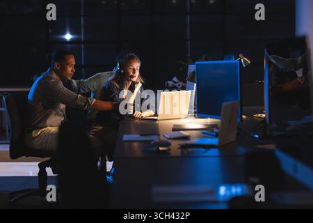 Colleagues collaborating on laptop in modern office during late-night work session Stock Photo