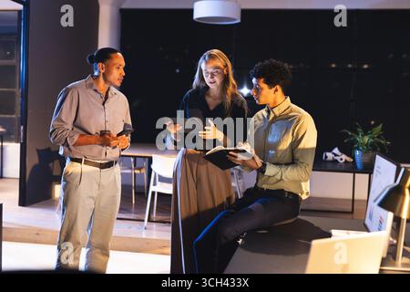 Business team collaborating on digital devices in modern office at night Stock Photo