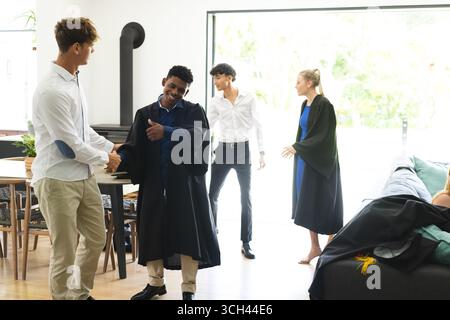 Teen graduates celebrating at home, shaking hands and smiling with friends Stock Photo