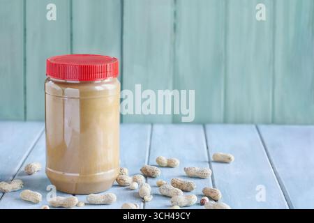 Front view of a full jar of peanut butter over a blue table with copy space and green background. Selective focus with blurred background. Stock Photo