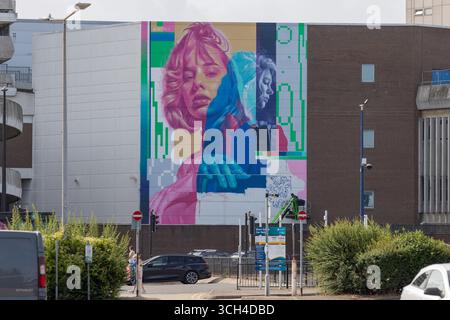 Southend on Sea, UK. 31st Aug, 2025. Artist on hydraulic lifts paint a large-scale mural in Southend-on-Sea featuring two abstract female portraits with glitch-inspired digital effects. Painted on a city building, the artwork blends vibrant pinks, reds, and blues in a contemporary urban style. The third day of City Jam. Many artists are still working on their murals. 2025 is the fourth year the event has been held. Penelope Barritt/17�Թ����� Live News Stock Photo