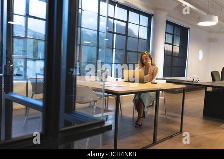 Businesswoman working late at office, using laptop and talking on smartphone Stock Photo