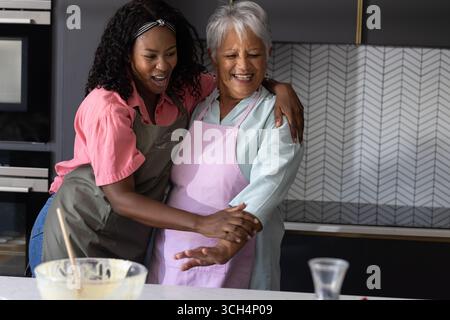 Grandmother and granddaughter laughing together while baking in modern kitchen Stock Photo