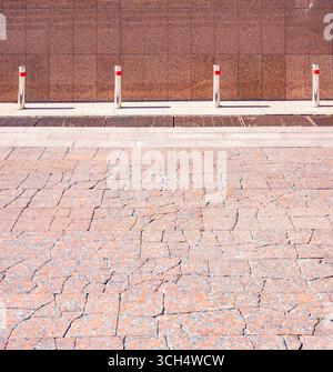 Cracked granite tiles form a pavement with metallic bollards and a granite wall in the background, creating a contrast between new and old, safety and Stock Photo