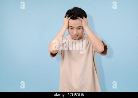 A young man standing in thoughtful pose, gesturing with his hand against a blue backdrop Stock Photo