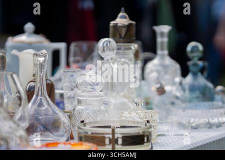 Flea market vintage things counter with vintage glass bottles, goblets, carafe and and other old things. Different antiques on flea market. Stock Photo