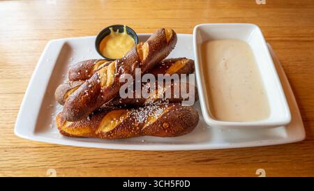 Golden-brown pretzel sticks, sprinkled with coarse salt, served on a white rectangular plate with two creamy dipping sauces. Stock Photo
