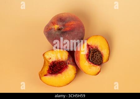 two peaches, one whole and one broken into 2 halves, one half whole and one half pitted, on a orange background Stock Photo