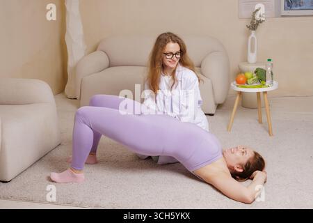 Smiling woman in sportswear doing rehabilitation exercises with trainer at home, physiotherapy, plus size fitness Stock Photo