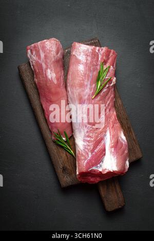 Uncooked pork tenderloin meat ready to cook on wooden background with rosemary, top view. Fresh juicy meat ready to cook, food concept. Stock Photo