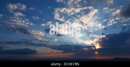 Panoramic view, beautiful sunset with heavy clouds and sun rays, blue-orange sky. Stock Photo