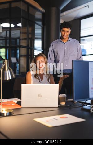 Colleagues discussing project on laptop in modern office during evening hours Stock Photo