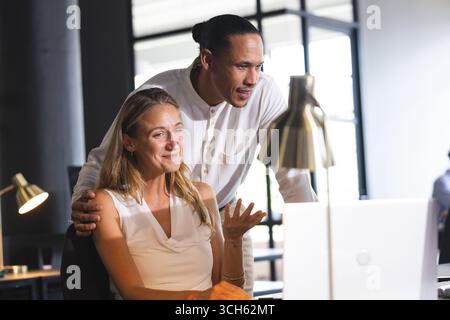 Colleagues collaborating on laptop in modern office, discussing project details Stock Photo