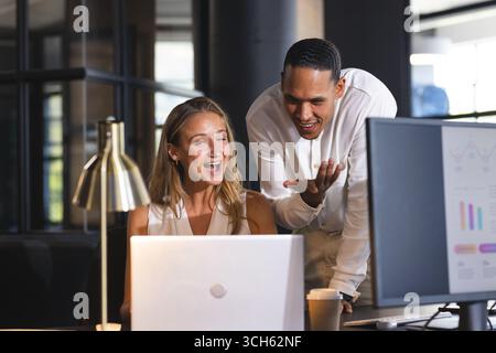 Colleagues collaborating on project, smiling at laptop screen in modern office Stock Photo