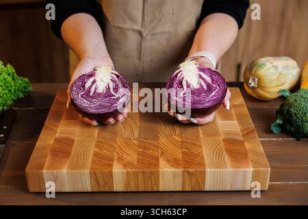 Woman holding two halves of red cabbage on wooden cutting board in cozy kitchen Stock Photo