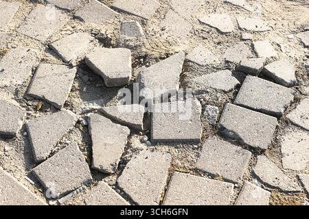 Broken paving stones on ground. Damaged sidewalk surface closeup. Old cracked pavement background. Urban construction problem. Rough outdoor texture. Stock Photo