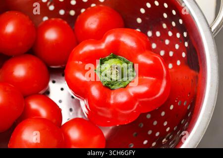 Fresh red bell pepper with tomatoes in colander. Healthy organic vegetables in kitchen. Natural diet ingredient for cooking. Closeup of ripe produce. Stock Photo