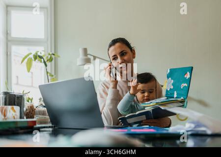 Female freelancer working with wireless technologies while holding son at home Stock Photo