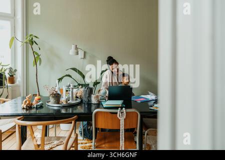 Female freelancer working on laptop while taking care of son at home Stock Photo