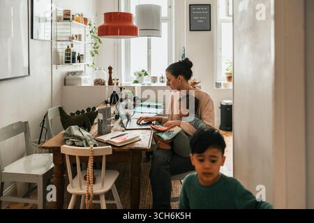 Mother working on laptop while sitting with baby boy at home Stock Photo