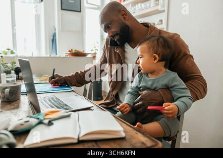 Cute baby boy sitting with father working from home Stock Photo