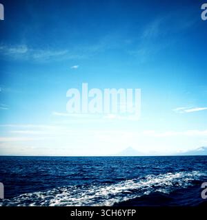 Blue seascape viewed from a moving boat in the Philippines, with a distant volcano rising above the horizon, captured on analog film. Stock Photo