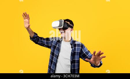 Joyful young guy using virtual reality headset, controlling cyber environment with moving gestures on orange background Stock Photo