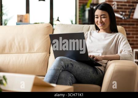 Female freelancer researching strategies and reviewing emails while managing tasks remotely. Asian entrepreneur excited after completing financial data and project presentation from home. Stock Photo