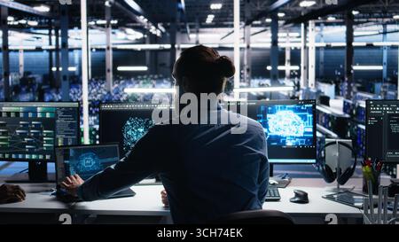 Server room software developer using AI to review infrastructure diagnostics. IT employee in data center analyzing performance data using artificial intelligence technology on devices, camera A Stock Photo