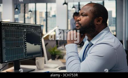 Close up of trader daydreaming, visualizing becoming rich after stock market speculations. African american man in prop firm office lost in thought, picturing prosperous trade Stock Photo