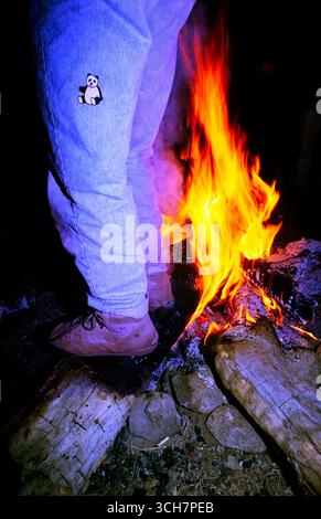 A single adult male stands a bit too close to the camp fire in order to stay warm on a cold winter night. Dragoon mountains, Arizona. USA Stock Photo