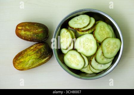 Fresh cucumber slices in a steel bowl and whole cucumber on wooden background. Top view Stock Photo