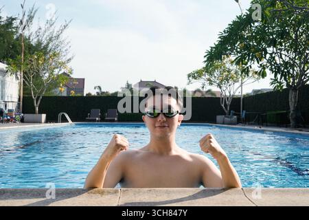 A young man wearing goggles poses confidently in a refreshing outdoor swimming pool Stock Photo