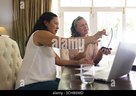 Asian woman and senior woman discussing project while using laptop at home. Technology, teamwork, collaboration, home office, multigenerational, women Stock Photo