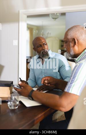 Senior men discussing plans at home, using smartphone and taking notes. Diverse Senior Friends, planning, technology, communication, collaboration, el Stock Photo
