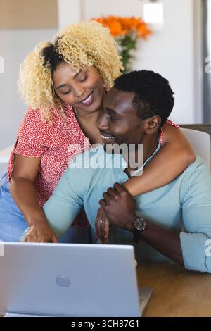 Happy couple embracing while using laptop at home, enjoying quality time together, copy space Stock Photo