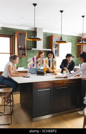 Collaborating on school project, teen friends using tablet and notes in kitchen Stock Photo