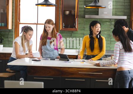 Teens collaborating on school project in kitchen, using tablet and papers Stock Photo