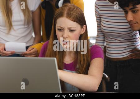 Teen girl concentrating on laptop with friends, collaborating on school project Stock Photo