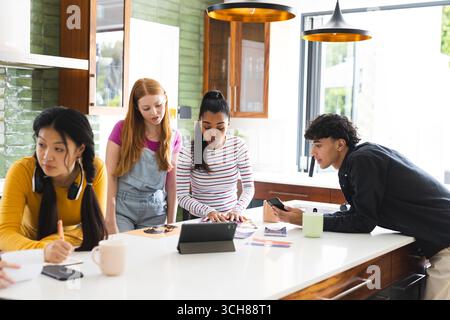 Teens collaborating on school project using tablet and smartphones in modern kitchen Stock Photo