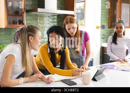 Teen girls collaborating on school project at home, using tablet and notes Stock Photo