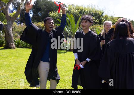 Graduating students holding diplomas and wearing caps, celebrating outdoors together Stock Photo